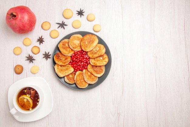 Bovenaanzicht thee en pannenkoeken plaat van pannenkoeken met granaatappel een kopje kruidenthee granaatappel en koekjes op de witte tafel