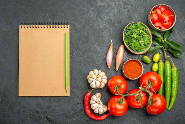 Bovenaanzicht tomaten notebook potlood naast de kommen van kleurrijke groenten specerijen kruiden