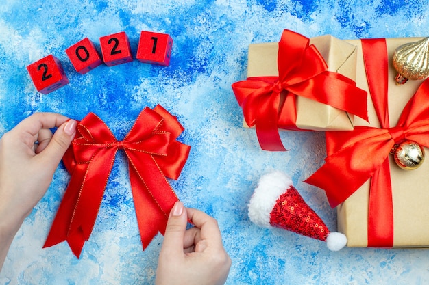 Bovenaanzicht vakantiegeschenken kleine kerstmuts houtblokken rode strik in vrouwelijke hand op blauw witte tafel