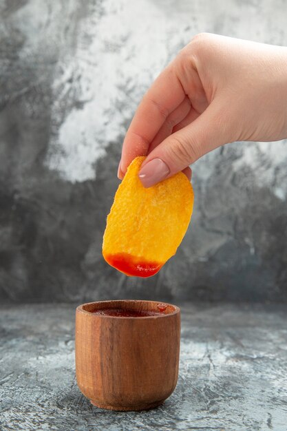 Bovenaanzicht van aardappelchips in een kleine ketchupkom op grijze achtergrond