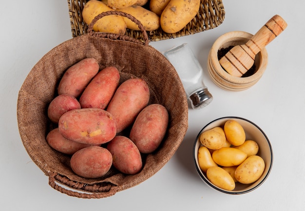 Bovenaanzicht van aardappelen in de mand en in plaat met zout zwarte peper op wit