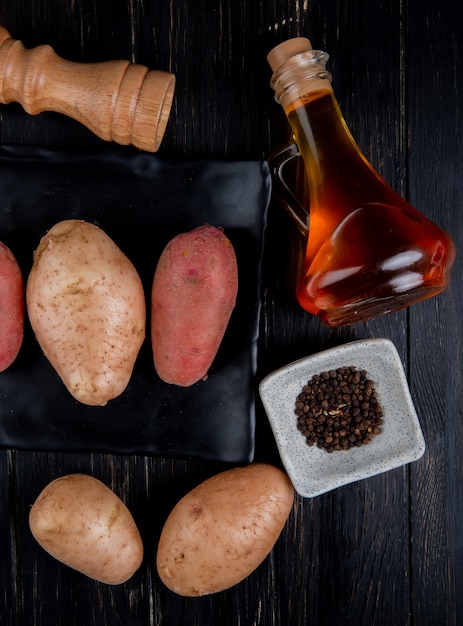 Bovenaanzicht van aardappelen in plaat met zwarte peper zaden gesmolten boter zout op houten oppervlak