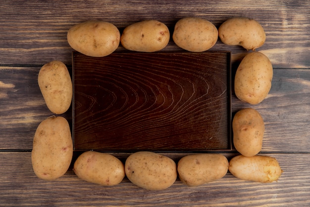 Gratis foto bovenaanzicht van aardappelen rond lege lade op houten oppervlak