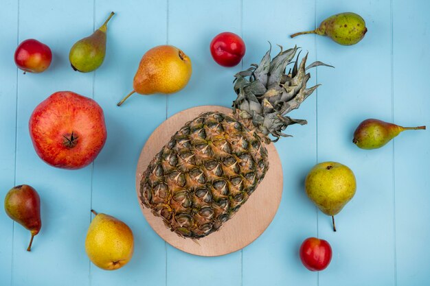 Bovenaanzicht van ananas op snijplank en patroon van fruit als granaatappel perzik pruim op blauwe ondergrond