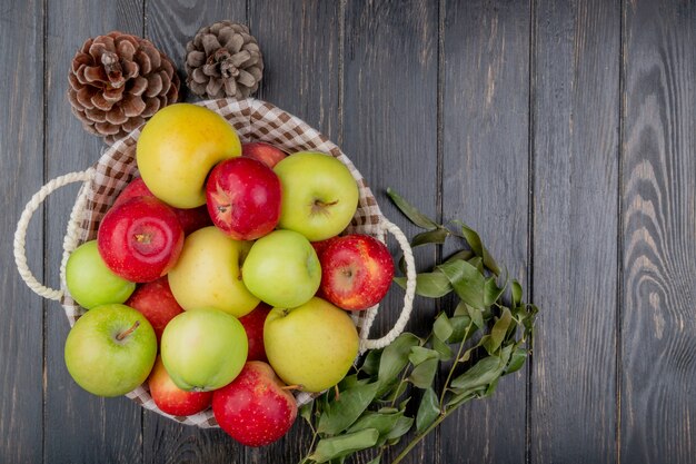 Bovenaanzicht van appels in mand met dennenappel en bladeren op houten achtergrond met kopie ruimte