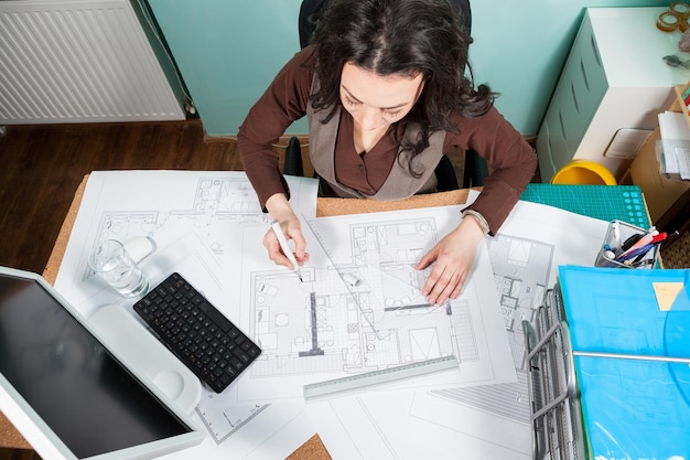 Bovenaanzicht van architect aan het werk aan haar bureau met blauwdrukken voor haar. Werken aan nieuwe projecten. Architectuur en design