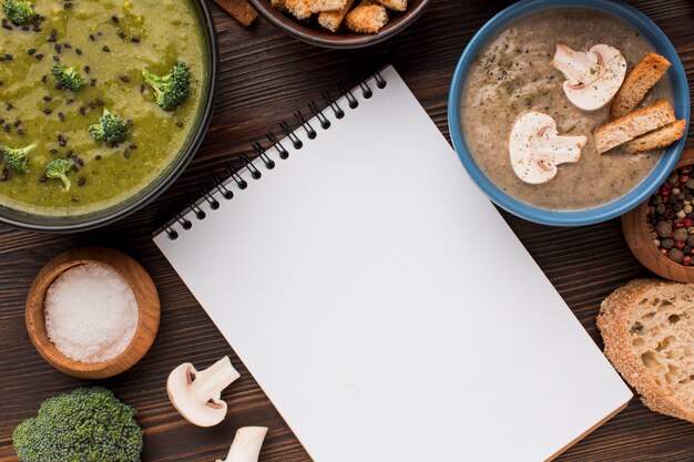 Bovenaanzicht van assortiment winter champignons en broccoli soepen met notebook