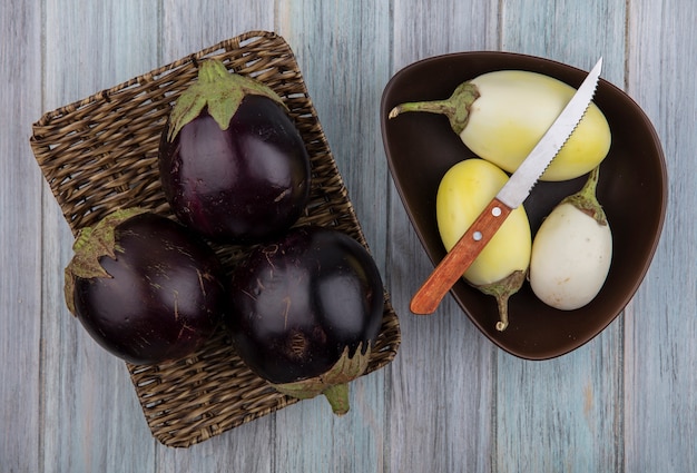 Bovenaanzicht van aubergines in mand plaat met gele en witte met mes in kom op houten achtergrond