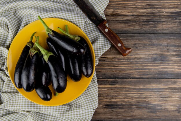 Bovenaanzicht van aubergines in plaat met mes op doek aan de linkerkant en houten achtergrond met kopie ruimte