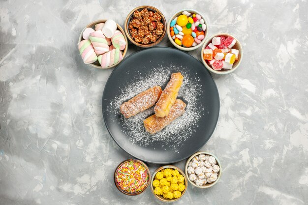 Bovenaanzicht van bagels met suiker in poedervorm met snoepjes en marshmallows op witte ondergrond