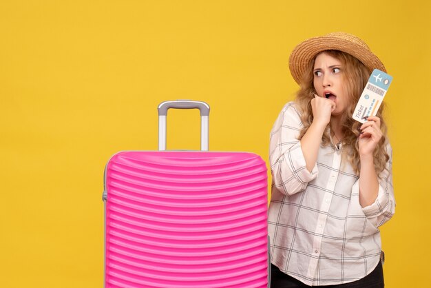 Bovenaanzicht van bang jonge dame met hoed met kaartje en permanent in de buurt van haar roze tas