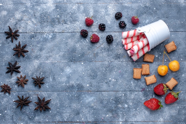 bovenaanzicht van bessen en koekjes met roze stoksuikergoed op helder bureau, het koekjeskoekje van de fruitbes