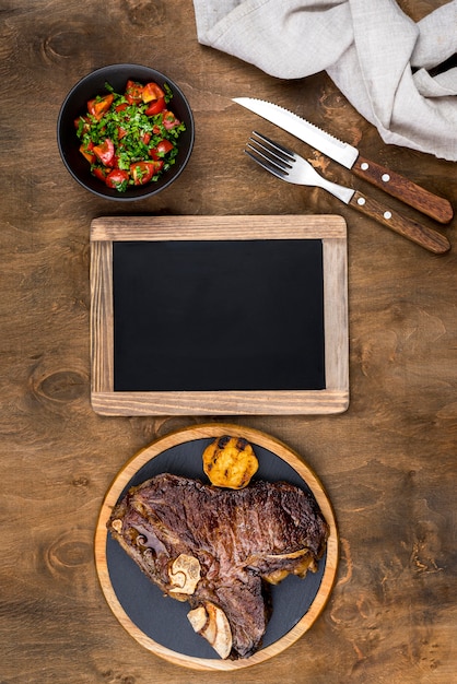 Gratis foto bovenaanzicht van biefstuk op plaat met salade en schoolbord