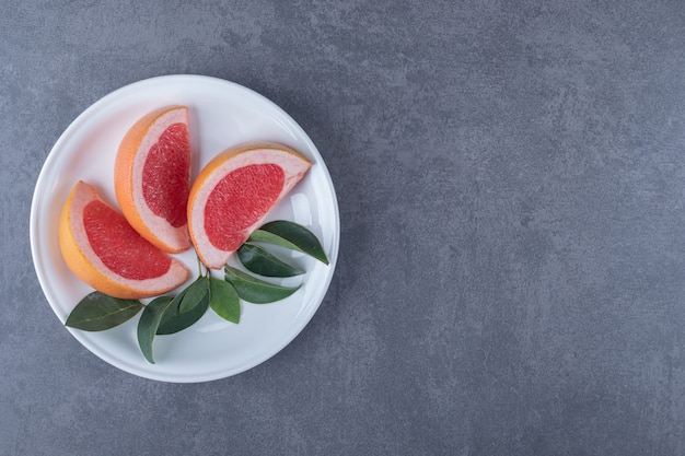 Gratis foto bovenaanzicht van biologische grapefruit plakjes en bladeren op een witte plaat.