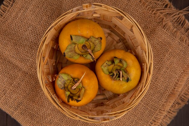 Bovenaanzicht van biologische kaki fruit op een emmer op een zakdoek op een houten tafel