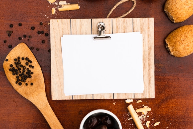 Bovenaanzicht van blanco wit papier met klembord; bun; broodstengels; peperbollen met spatel op houten bureau