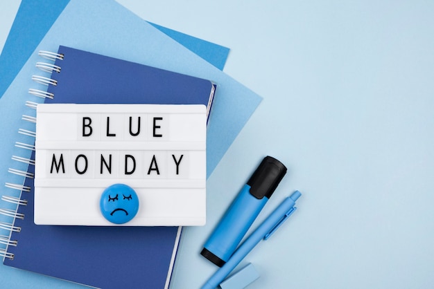 Bovenaanzicht van blauwe maandag lichtbak met droevig gezicht en notitieboekje