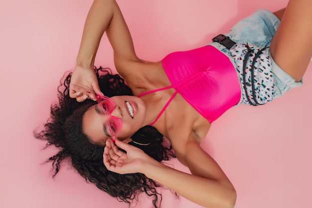 Bovenaanzicht van bovenaf aantrekkelijke vrouw liggend in stijlvolle zomer outfit roze top, korte broek op roze muur