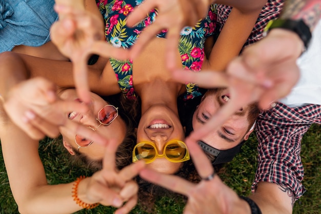 Gratis foto bovenaanzicht van bovenaf op kleurrijke stijlvolle gelukkig jong gezelschap van vrienden liggend op gras in park, man en vrouw samen plezier