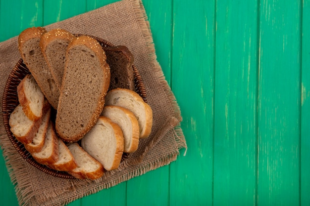 Bovenaanzicht van brood als gezaaide bruine maïskolf en stokbrood plakjes in mand op zak op groene achtergrond met kopie ruimte