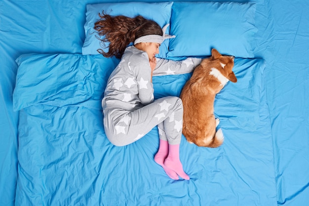 Bovenaanzicht van brunette jonge Europese vrouw in pyjama slaapt samen met favoriete huisdier ziet zoete dromen voelt comfortabel heeft gezonde slaap houdingen op bed. Mensen ontspanning dieren bedtijd concept