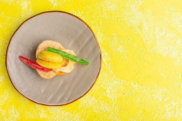 Bovenaanzicht van cakeplak met macaron en marmelade binnen plaat op geel oppervlak