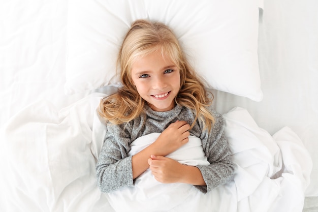 Gratis foto bovenaanzicht van charmante blonde meisje glimlachend en liggend in bed