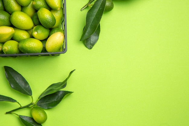 Bovenaanzicht van citrusvruchten, groene bladeren en mand met citrusvruchten op tafel