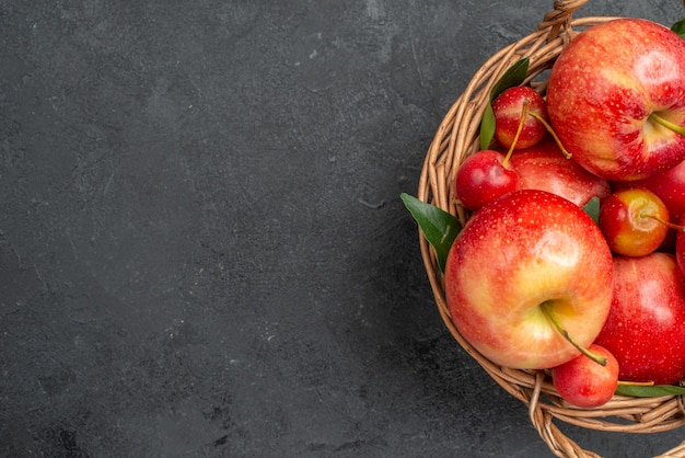 Bovenaanzicht van close-up fruit, kersen en appels in de houten mand op de donkere tafel