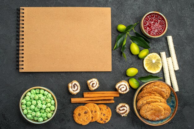 Bovenaanzicht van close-up snoepjes jam koekjes kleurrijke snoepjes kaneelstokjes crème notebook