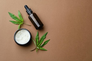 Bovenaanzicht van cosmetische oliecrème voor cannabis in een potfles en een blad van een groene plant natuurlijke cosmetica op bruine achtergrond platliggende kopieerruimte