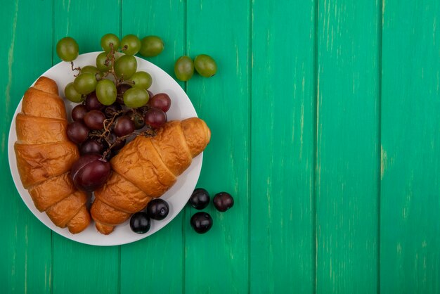 Bovenaanzicht van croissants en druivenmost in plaat op groene achtergrond met kopie ruimte