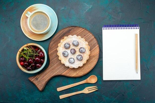 Bovenaanzicht van cupcake met kersen en suikerpoeder naast hete koffie en notitieboekje