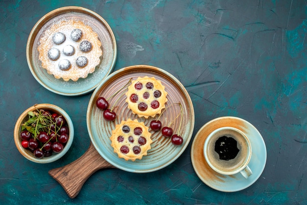 Gratis foto bovenaanzicht van cupcakes met kersen naast americano op blauw,