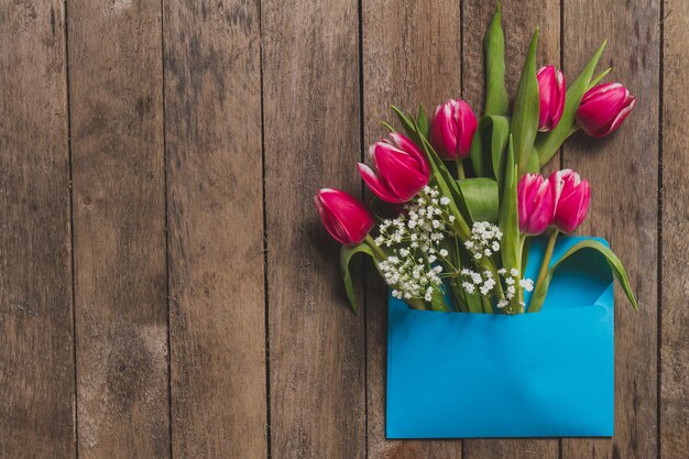 Bovenaanzicht van de blauwe envelop met bloemen op houten tafel