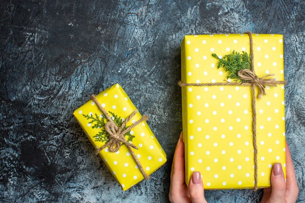 Bovenaanzicht van de hand met een van de gele kerstgeschenkdozen op een donkere achtergrond