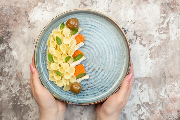 Bovenaanzicht van de hand met heerlijke pastamaaltijd geserveerd met groenten op een blauw bord op een mix van kleuren achtergrond met vrije ruimte
