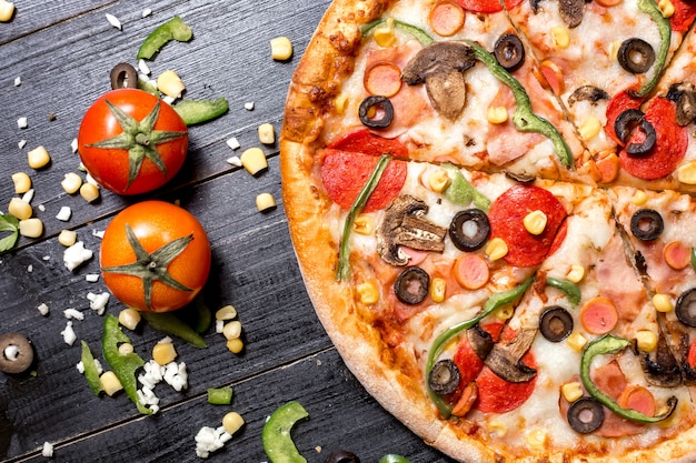 Bovenaanzicht van de helft van de pepperoni pizza geplaatst naast tomaten, kaas, maïs en paprika