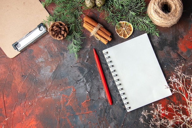 Bovenaanzicht van dennentakken en gesloten spiraal notebook kaneel limoenen conifer kegel een bal van touw op rode achtergrond