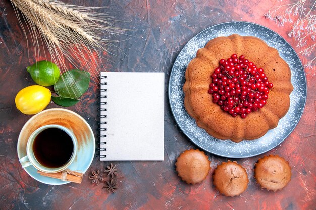 Bovenaanzicht van dichtbij een kopje thee een kopje thee wit notitieboekje cupcakes cake met bessen citroenen