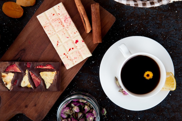 Bovenaanzicht van donkere en witte chocoladerepen met kaneelstokjes op een houten bord en een kopje thee op rustiek