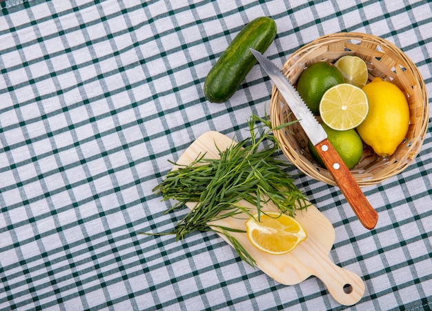 Bovenaanzicht van dragon greens op een houten keukenbord met plakjes citroen met een emmer verse citroenen met mes op gecontroleerd tafellaken oppervlak