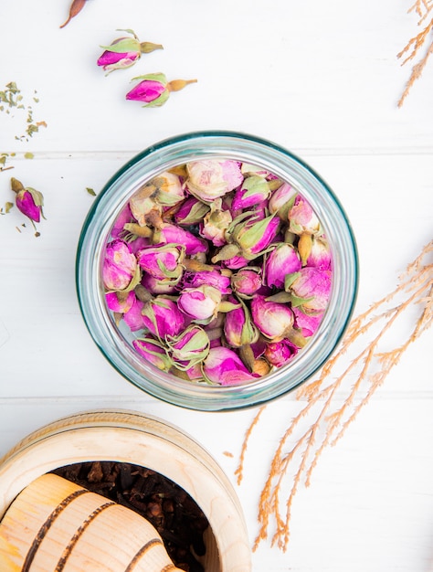 Bovenaanzicht van droge thee roos toppen in een glazen pot met zwarte peper in een houten vijzel op wit hout