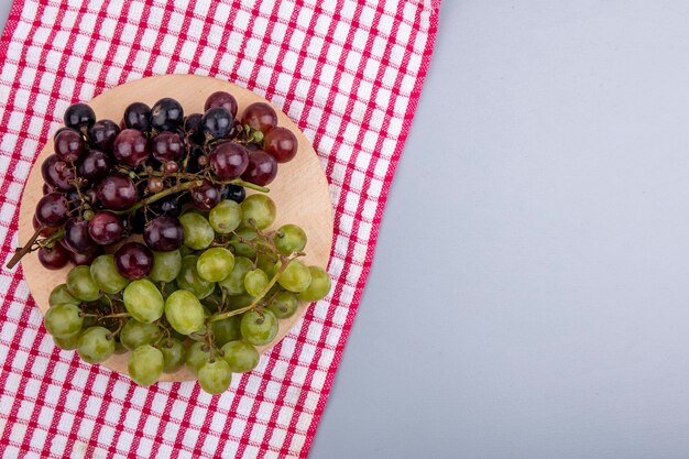 Bovenaanzicht van druiven op snijplank op geruite doek en op grijze achtergrond met kopie ruimte