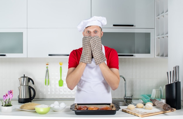 Bovenaanzicht van een bange chef-kok met een houder die achter de tafel staat met gebakeierenrasp erop in de witte keuken