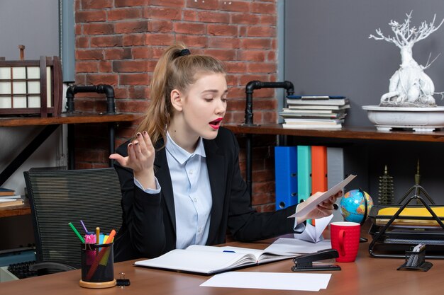 Bovenaanzicht van een bezorgde vrouw die aan een tafel zit en een document op kantoor vasthoudt