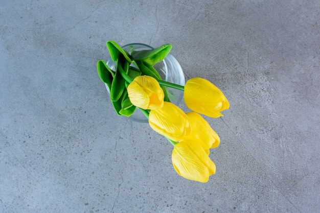 Bovenaanzicht van een boeket gele tulpen in een glazen vaas op het grijs