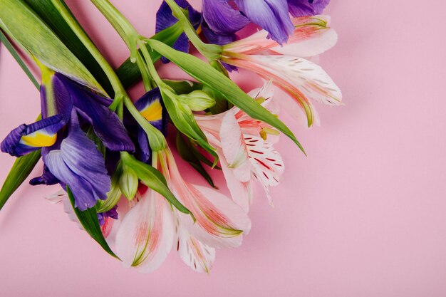 Bovenaanzicht van een boeket van donkerpaarse en roze kleur iris en alstroemeria bloemen op roze achtergrond