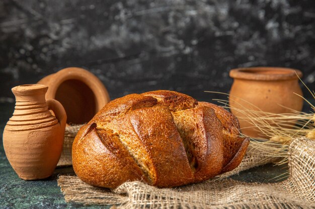 Bovenaanzicht van een brood van dieet zwart brood op bruine handdoek en pottenbakkerijen op donkere ondergrond