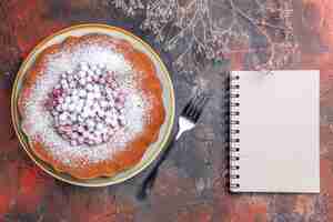 Gratis foto bovenaanzicht van een cake een vork wit notitieboekje naast de smakelijke cake met rode aalbessen